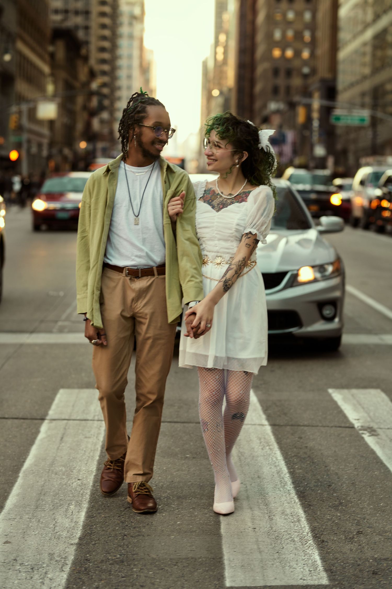 Two people walk together across a city crosswalk in casual attire during sunset hours. Engagement shoot Manhattan