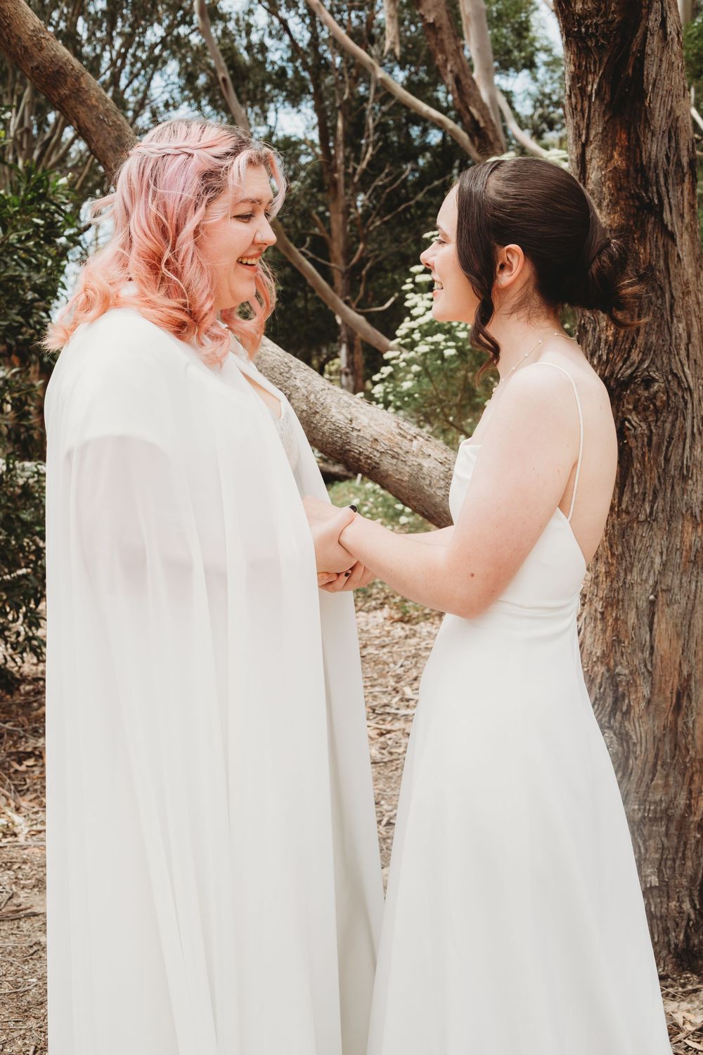 A romantic outdoor wedding photoshoot featuring two people in white dresses sharing tender moments among trees.