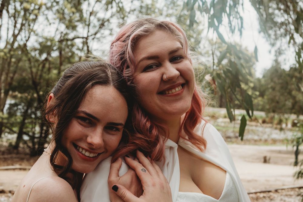 People laughing and embracing outdoors in natural setting with trees and sunlight filtering through branches.