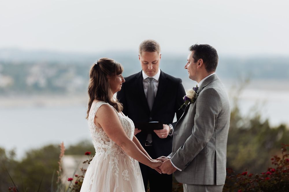 A wedding ceremony takes place on a hilltop overlooking a scenic waterfront vista.