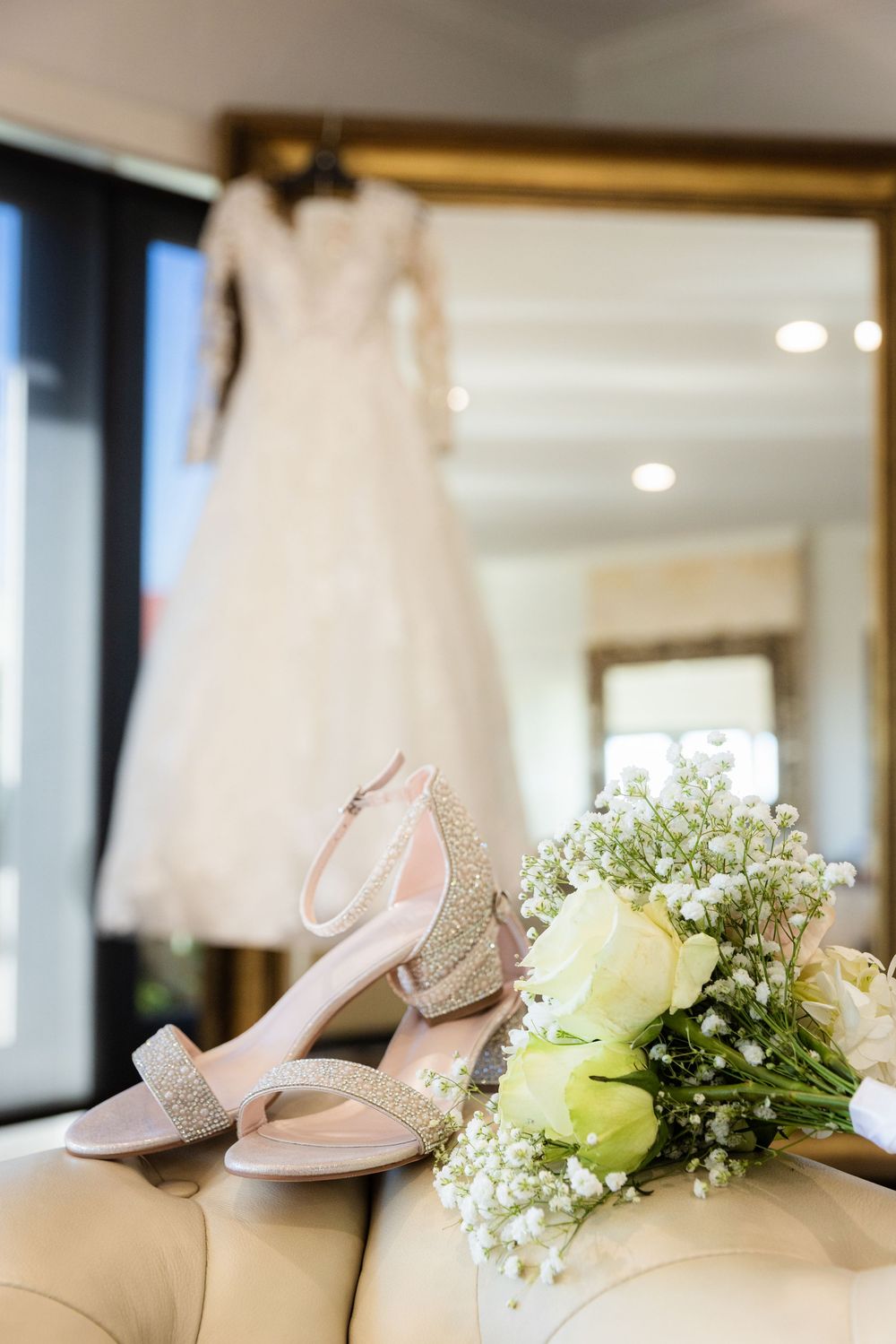 Elegant bridal shoes and a delicate white bouquet with roses and baby's breath rest against a beige surface.