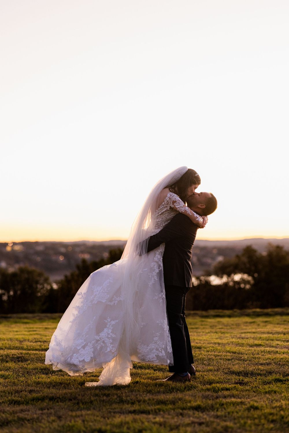 Romantic silhouette of bride and groom embracing on hilltop during golden sunset.