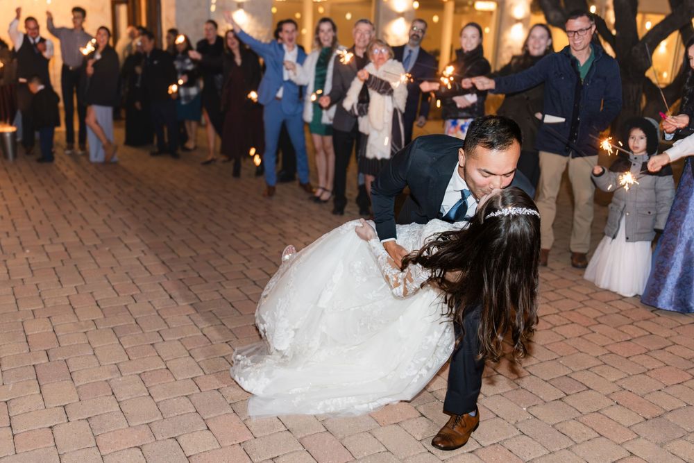 Reception guests dancing and celebrating on an outdoor brick-paved patio in the evening.