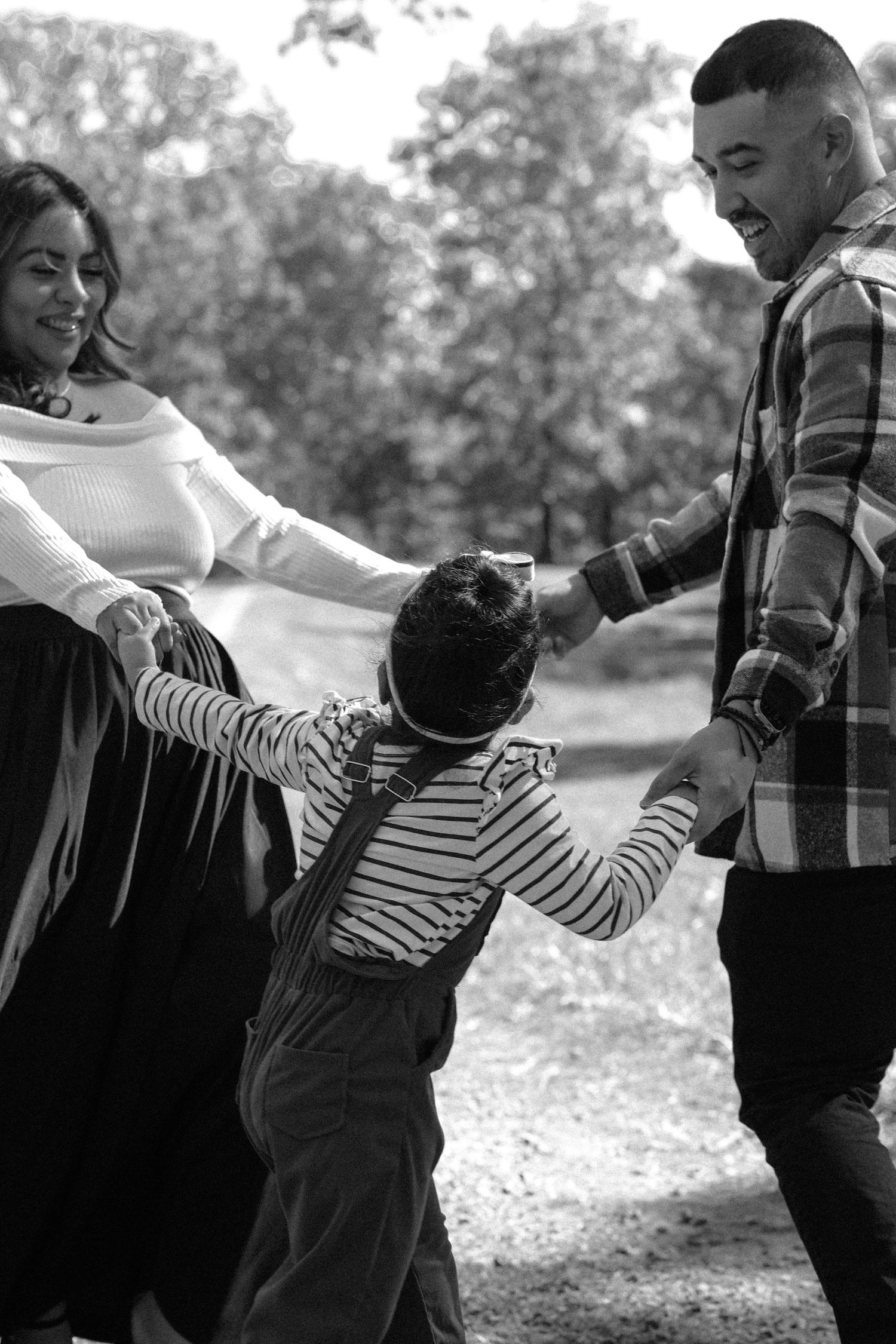 A family plays together and holds hands in a black and white candid moment outdoors in nature.