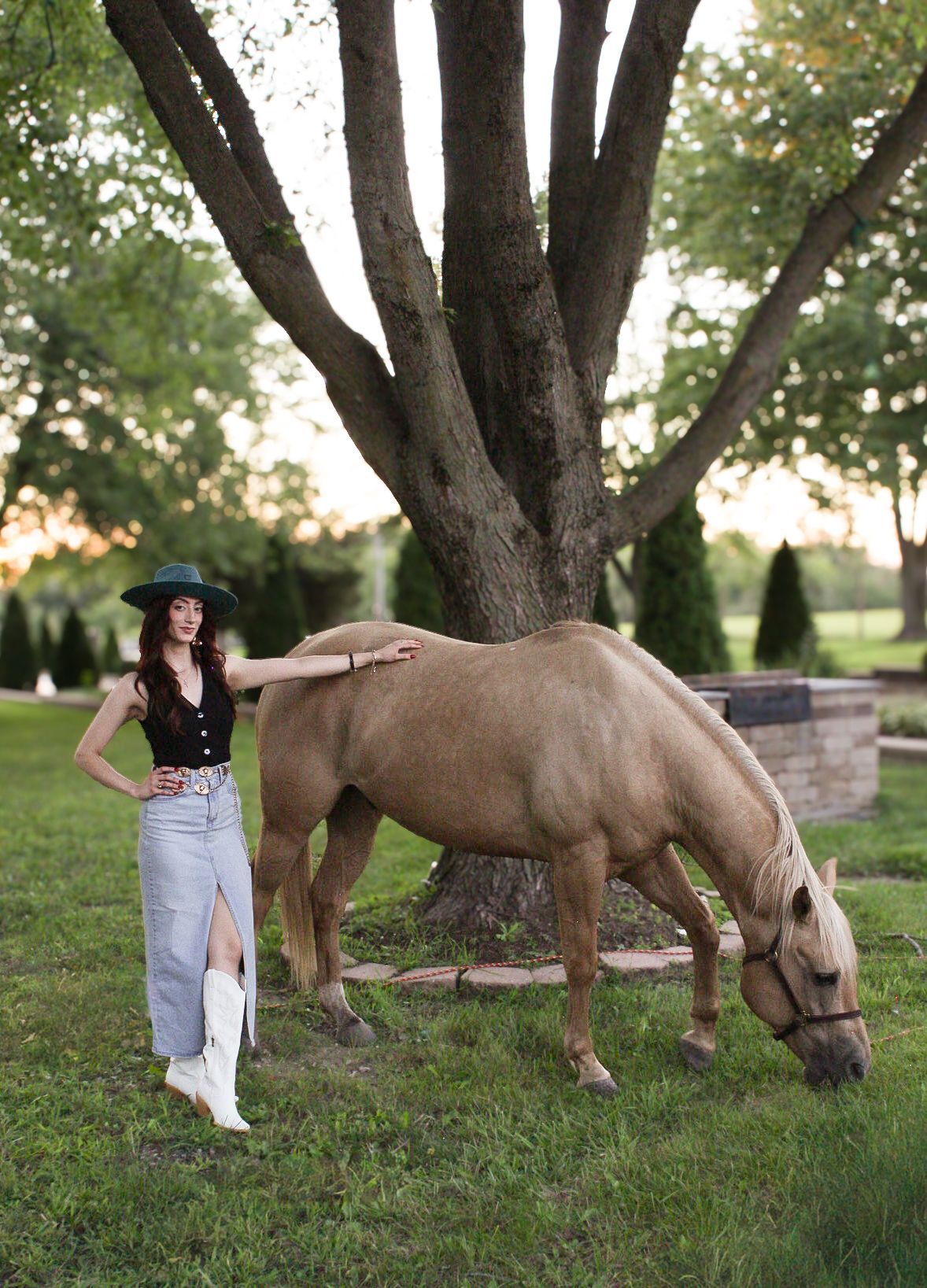 Outdoor photoshoot in a park with horses grazing on grass near trees.