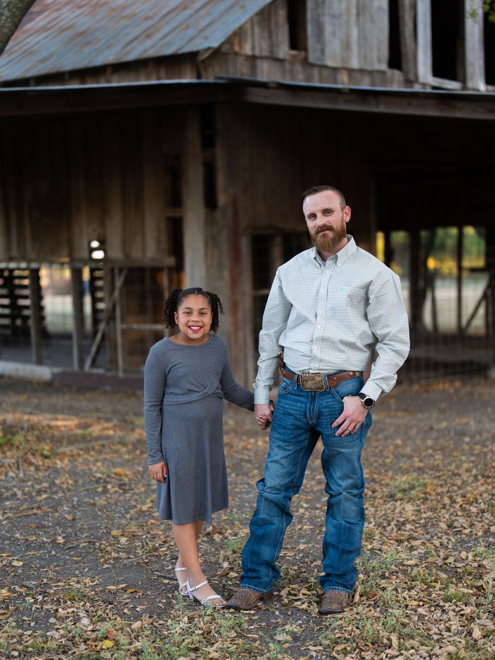 Father and daughter standing together outside rustic barn.