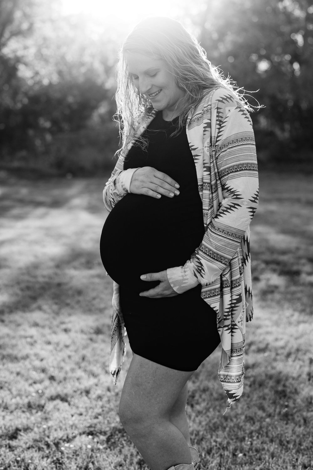 Expecting mother in black dress and patterned cardigan poses during golden hour maternity photoshoot.