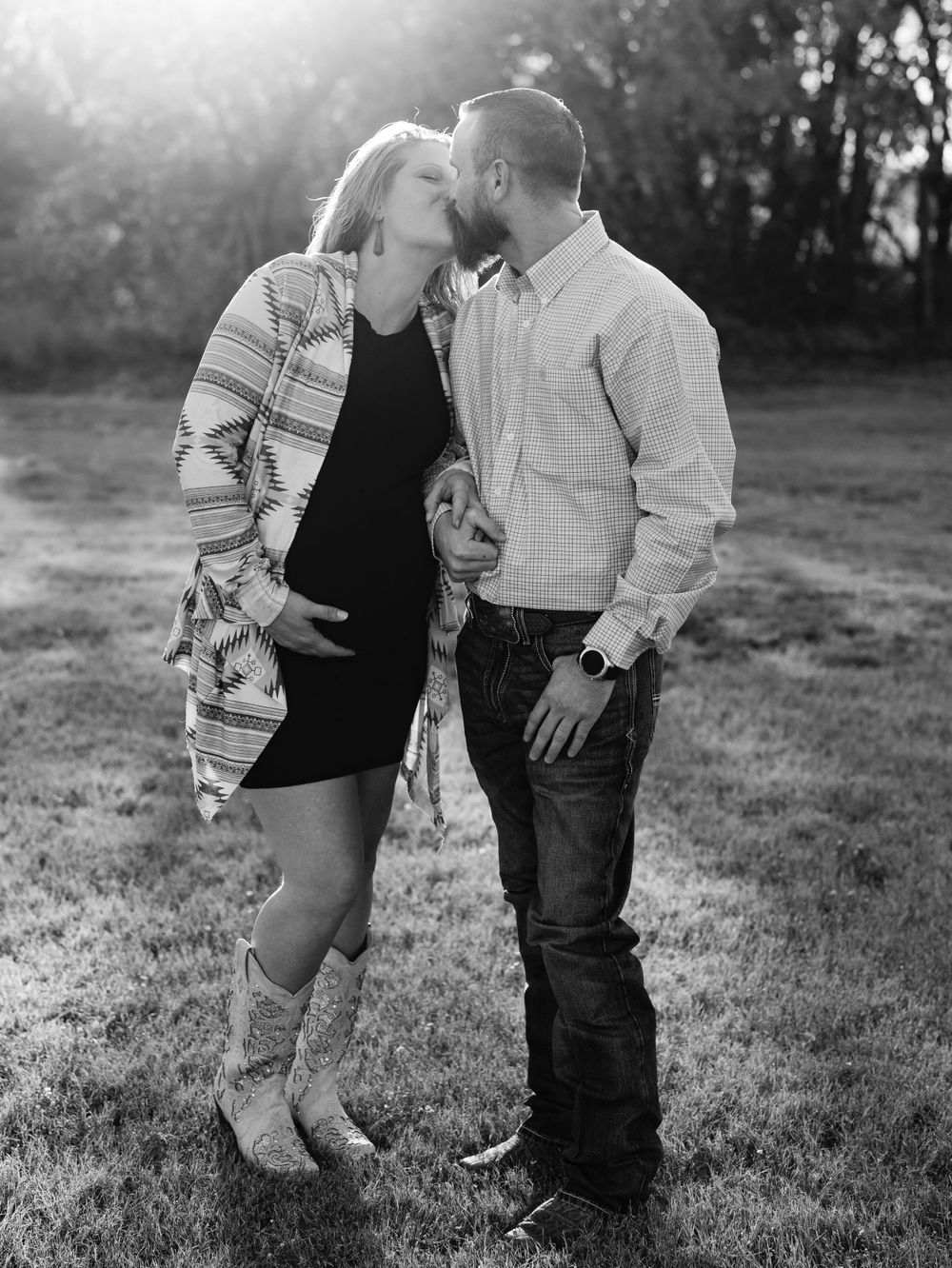Intimate moment between couple during maternity photoshoot outdoors at sunset.