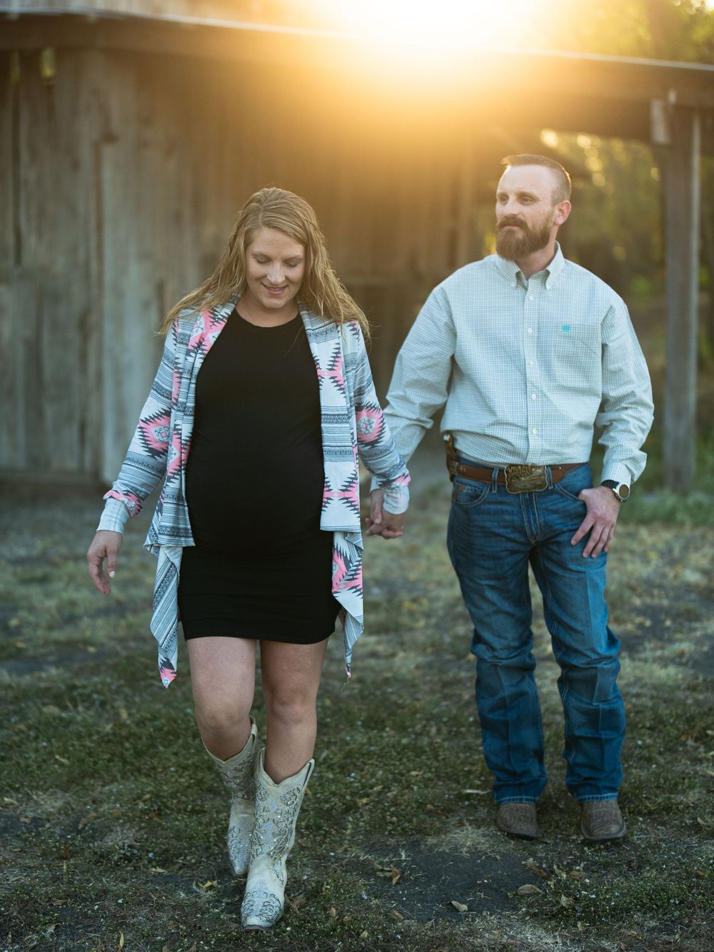 A casual outdoor portrait in front of a barn with someone wearing a floral cardigan and cowboy boots.