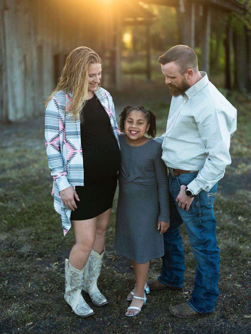 Family portrait at sunset by an old barn featuring coordinated casual country outfits.
