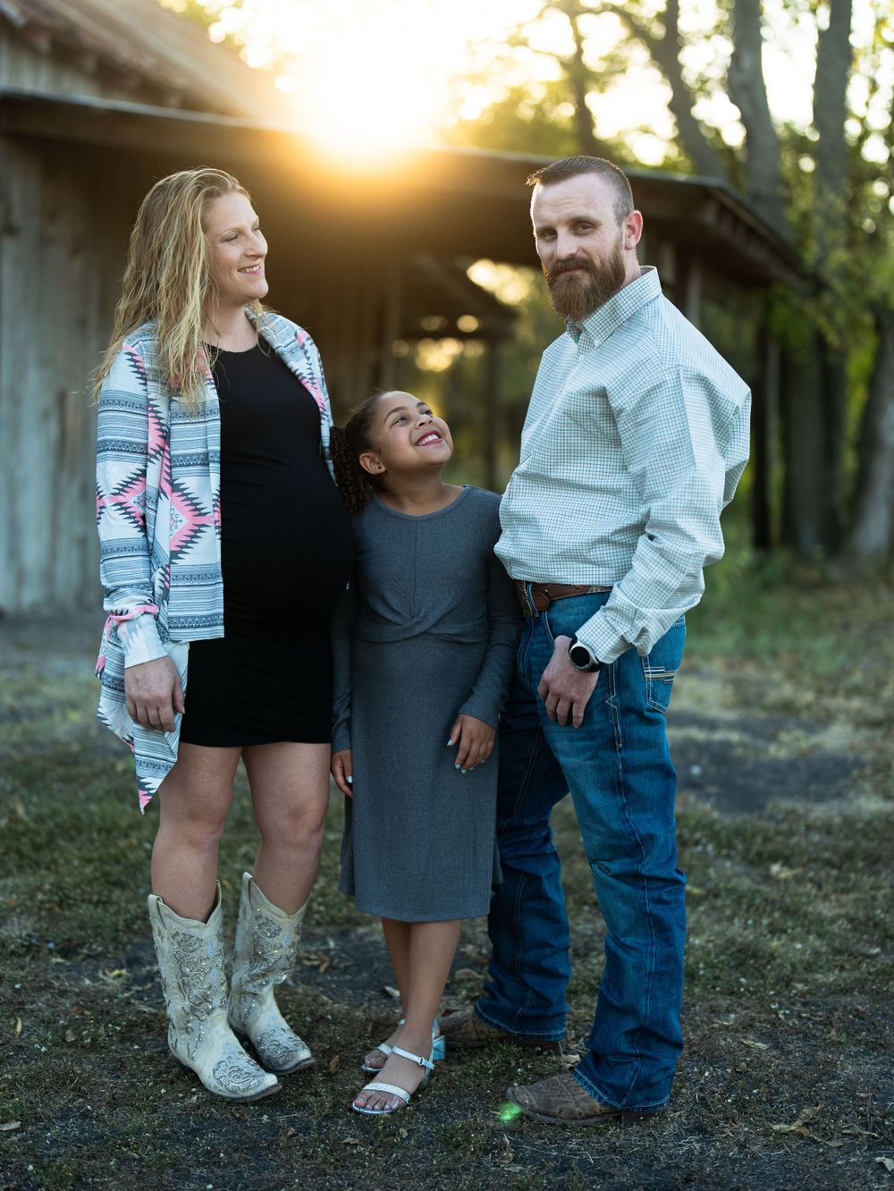 Happy family photo session outdoors with rustic barn and sunset backdrop.