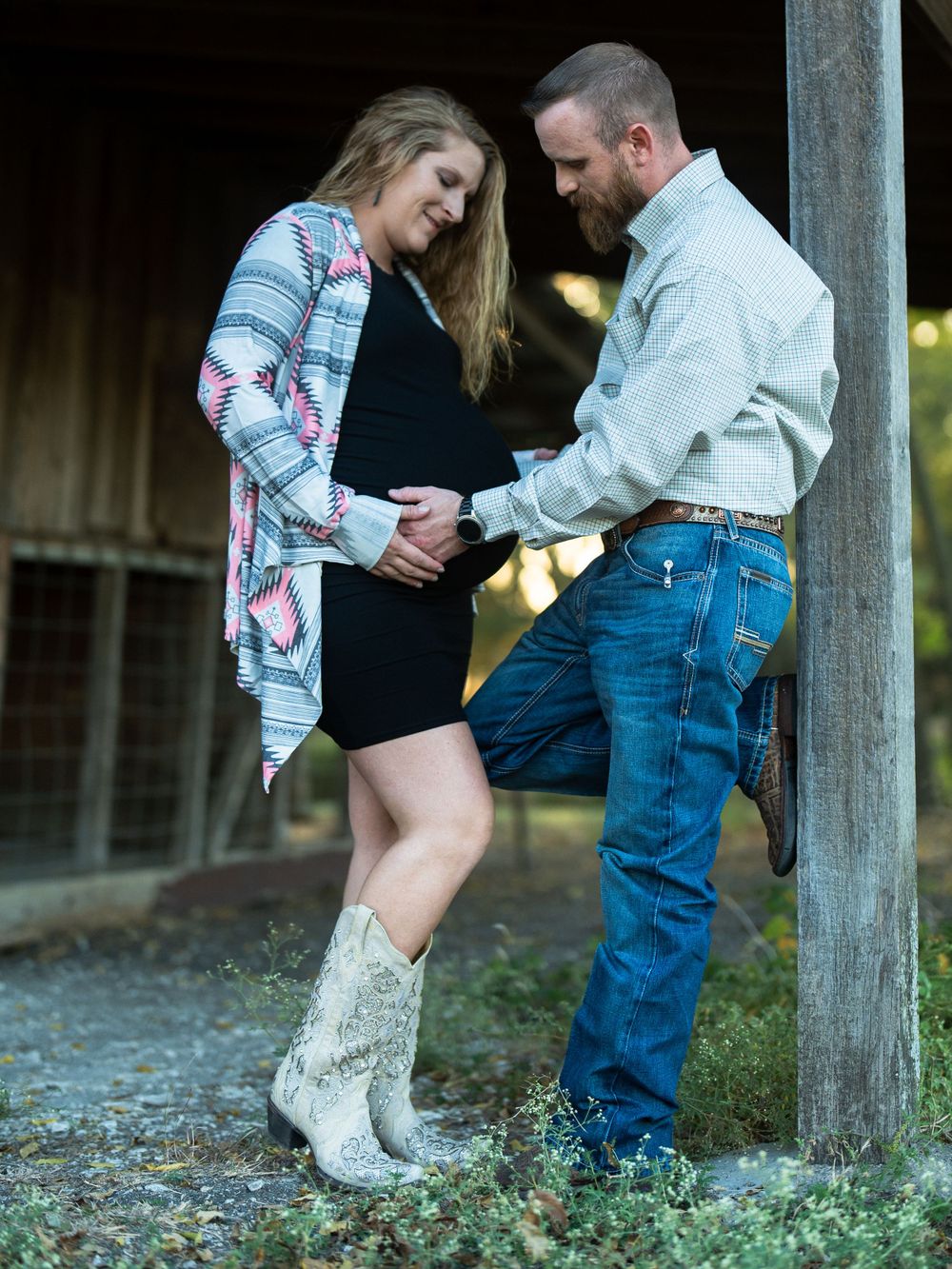 Intimate couple's portrait against a barn wall showing western boots and casual attire.