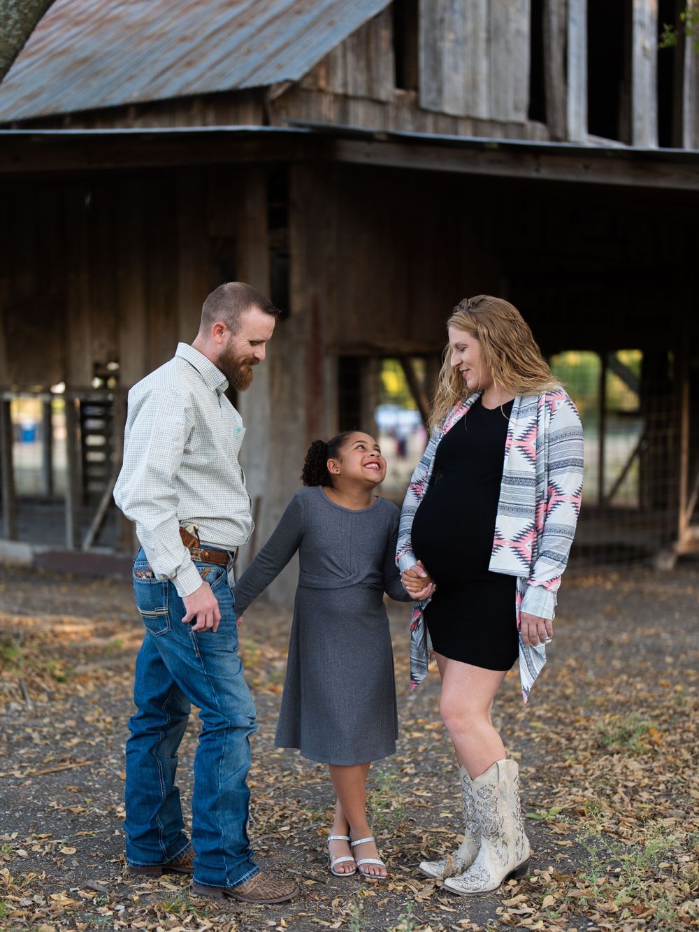 Family shares a joyful moment together on a rustic farm property during a casual outdoor photo session.