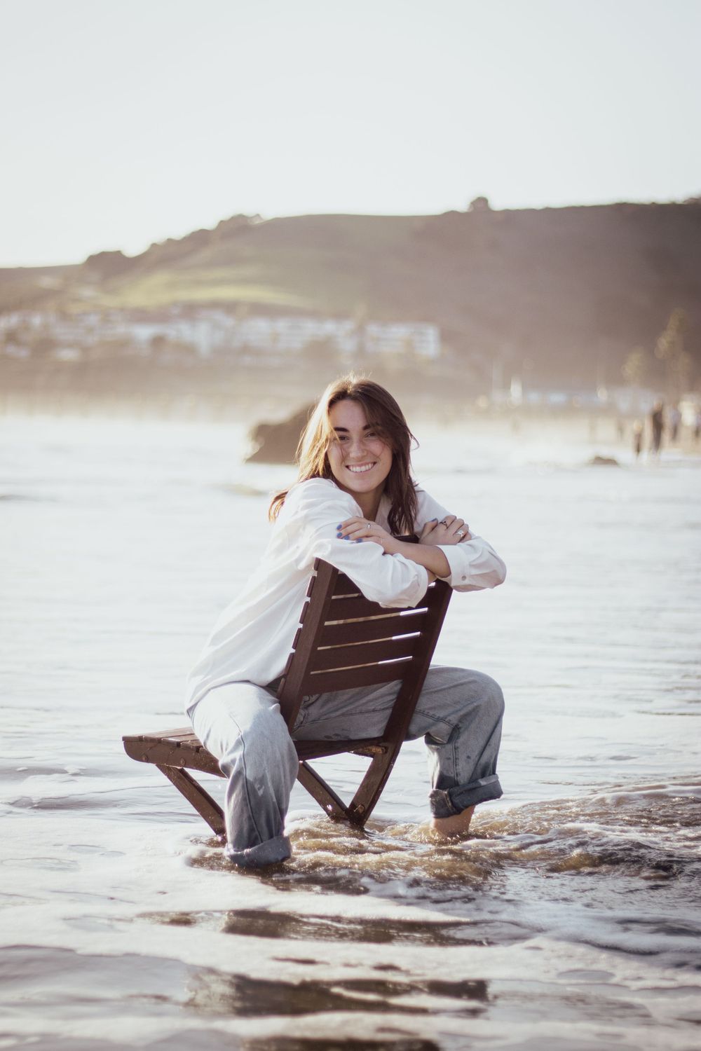 Person sitting in wooden chair at beach during sunset with waves in background.