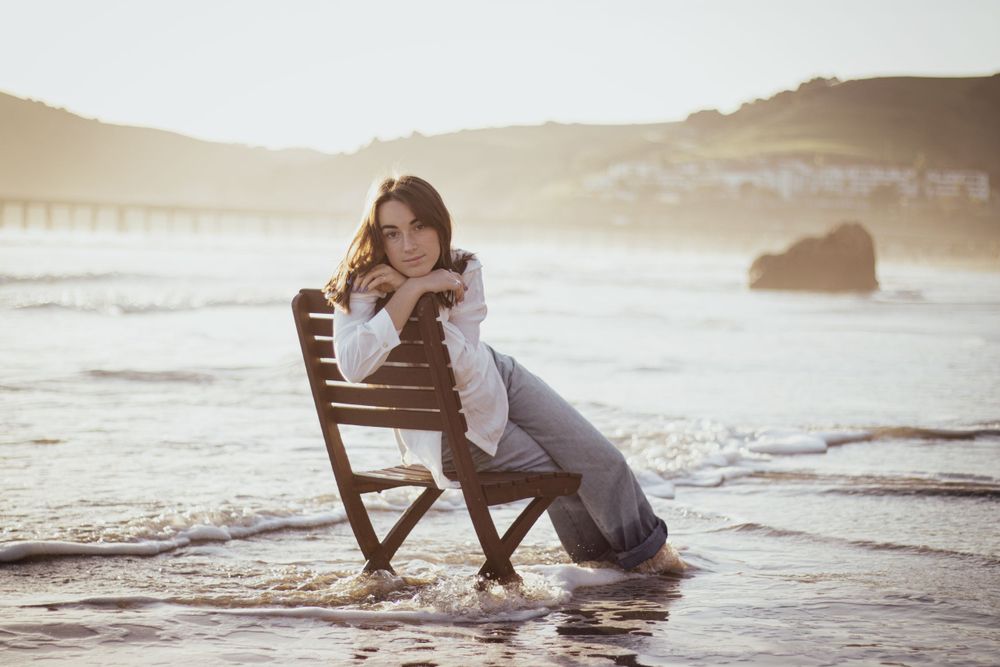 Figure lounging in wooden chair at beach during golden hour.