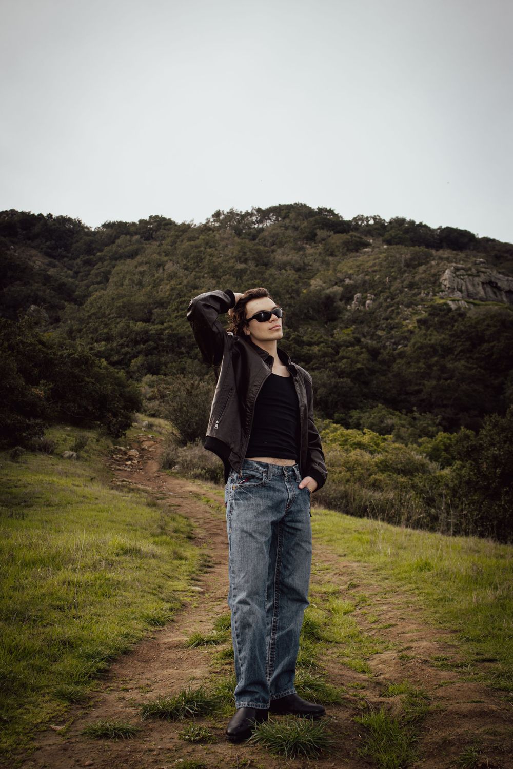 Figure in casual wear standing on a hiking trail against a backdrop of green hills.