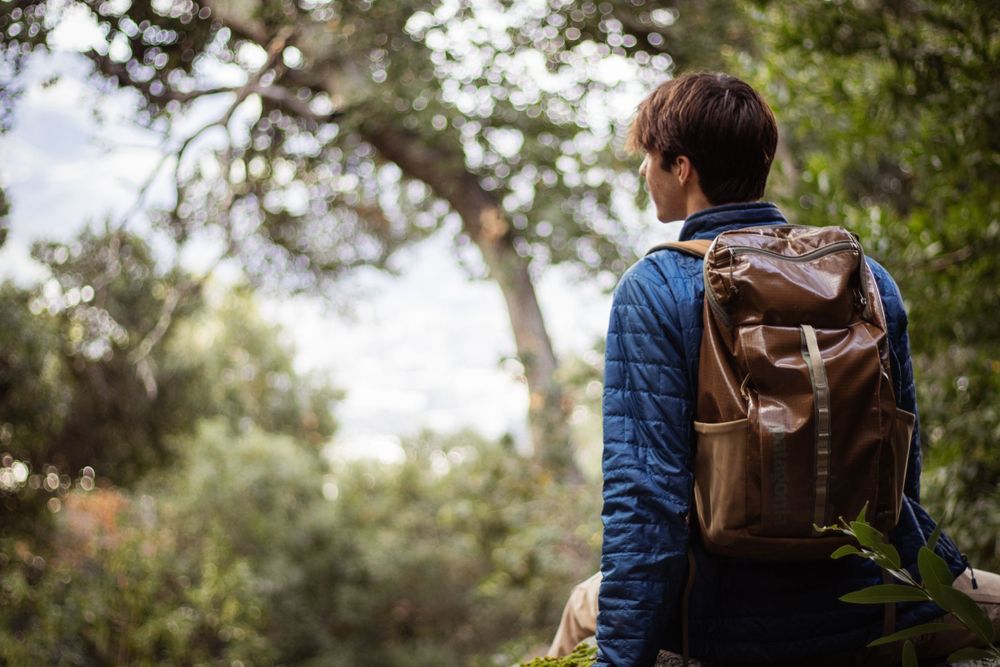 Hiker with leather backpack explores wooded trail during outdoor adventure.