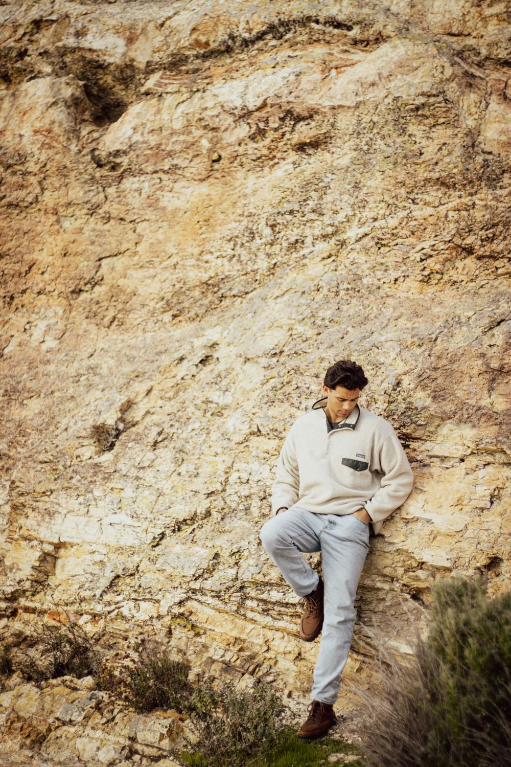 Figure in light sweater leans against rocky cliff face in outdoor setting.