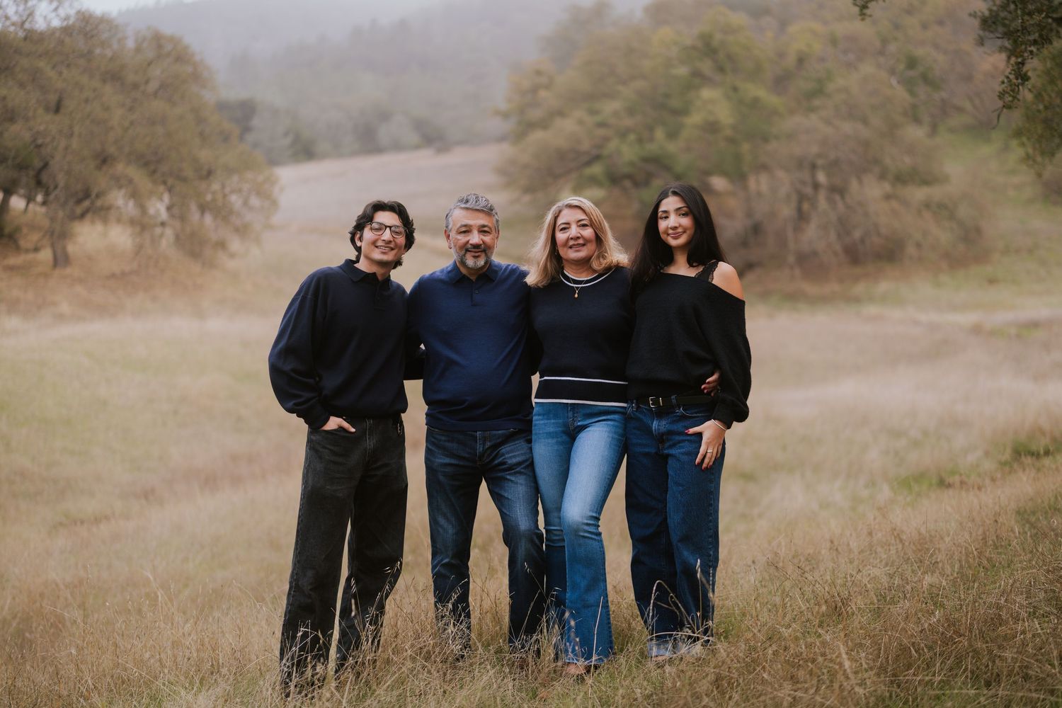 A group stands together in a golden field with misty mountains in the background during sunset.