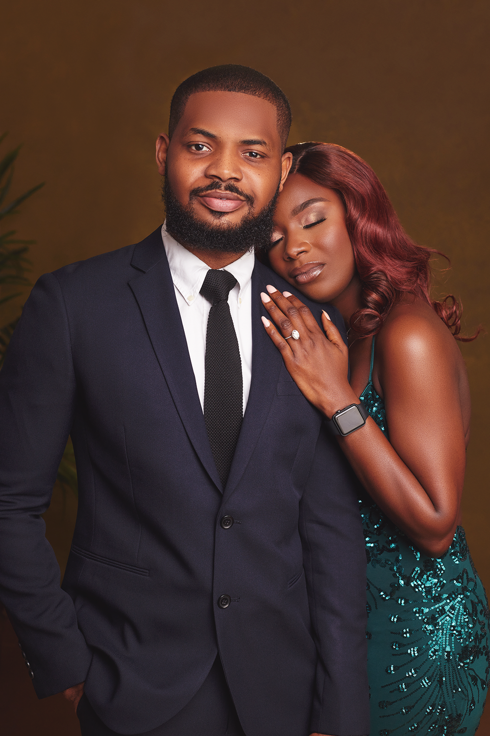 A romantic studio portrait of a couple in formal attire, with a sparkling emerald green dress and classic black suit.