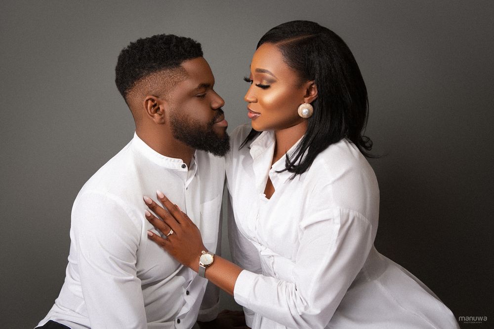 Romantic couple in matching white shirts pose intimately against dark gray studio background.