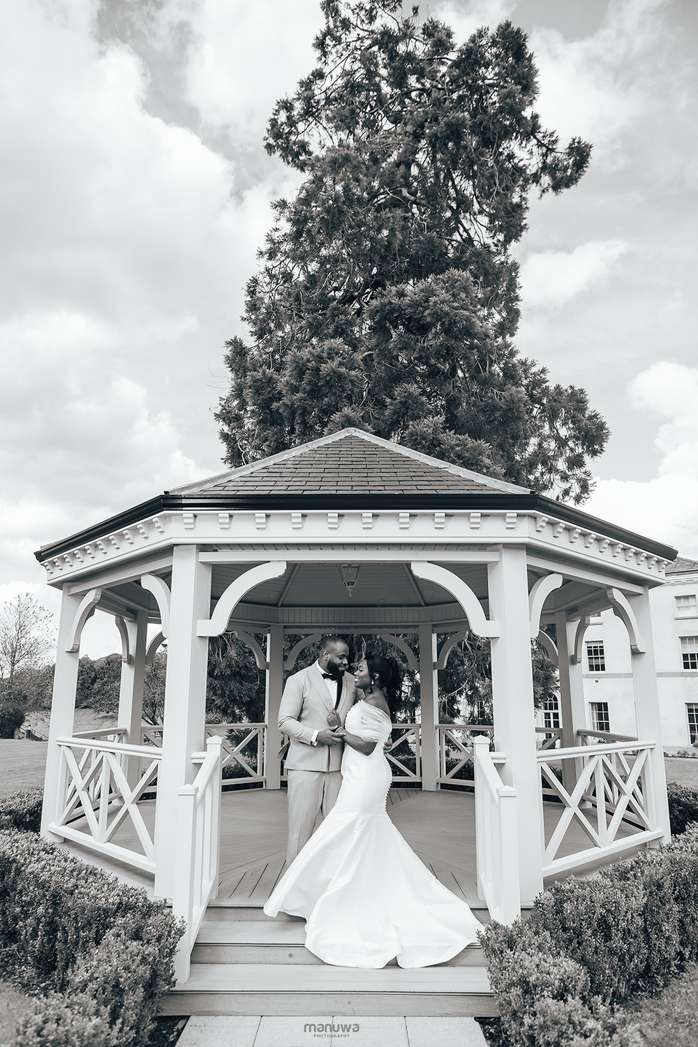 A romantic black and white wedding photo of a couple dancing in a white garden gazebo.