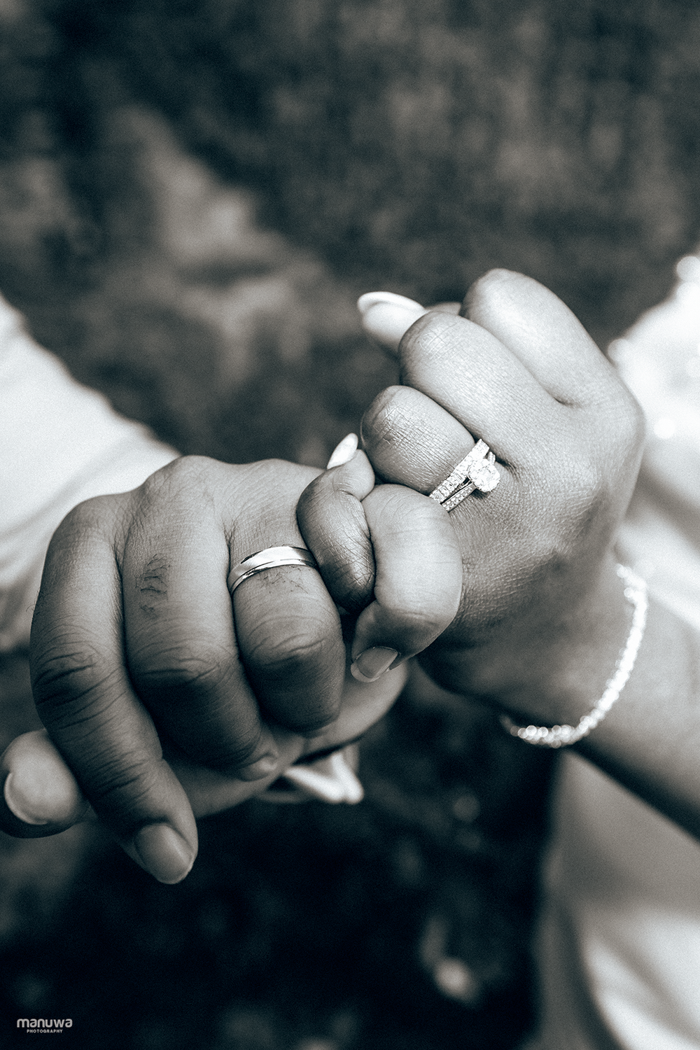 A close-up black and white photo of hands displaying wedding rings against a blurred background.
