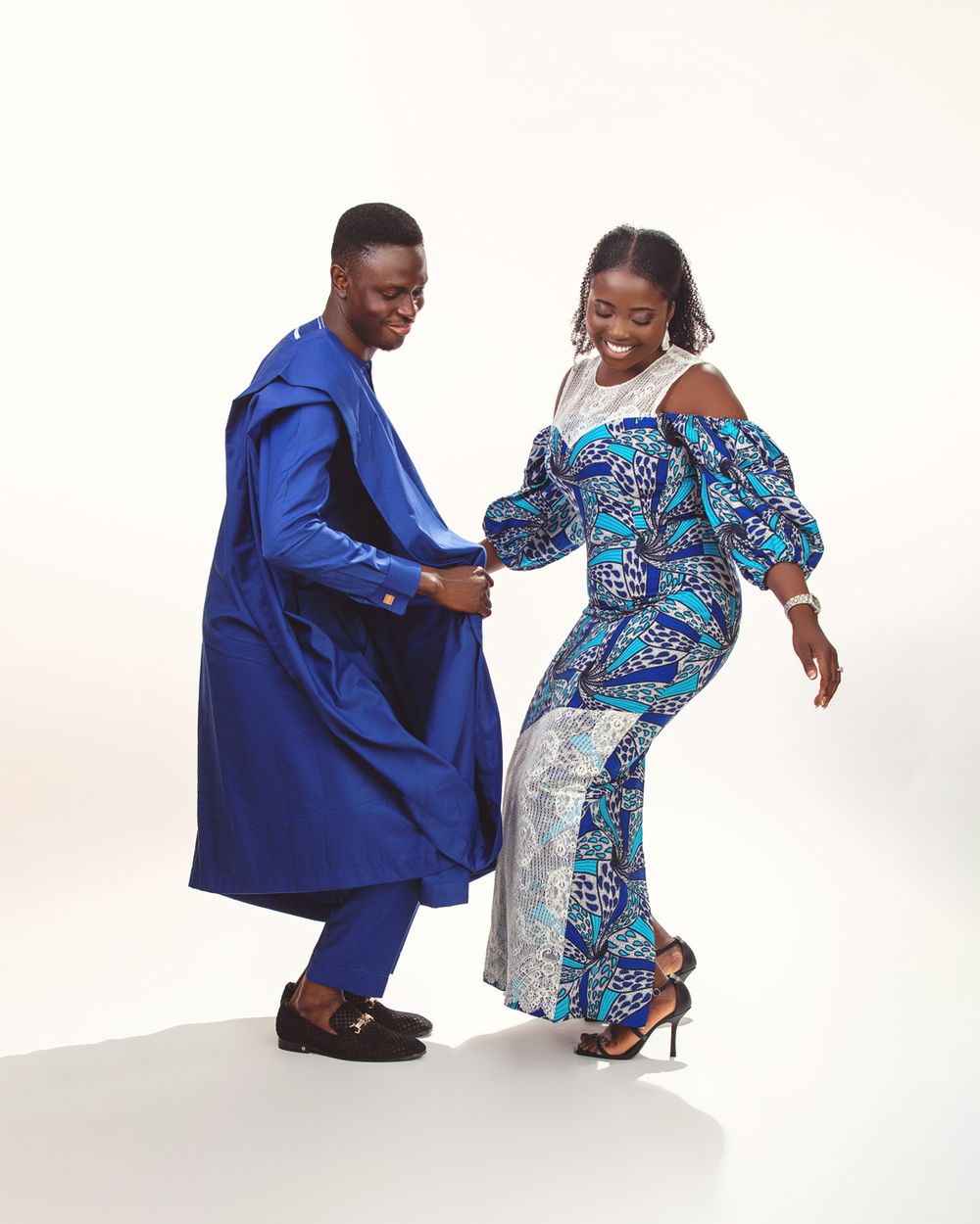 Two people in colorful outfits dance together against a white background, wearing blue and patterned clothing.