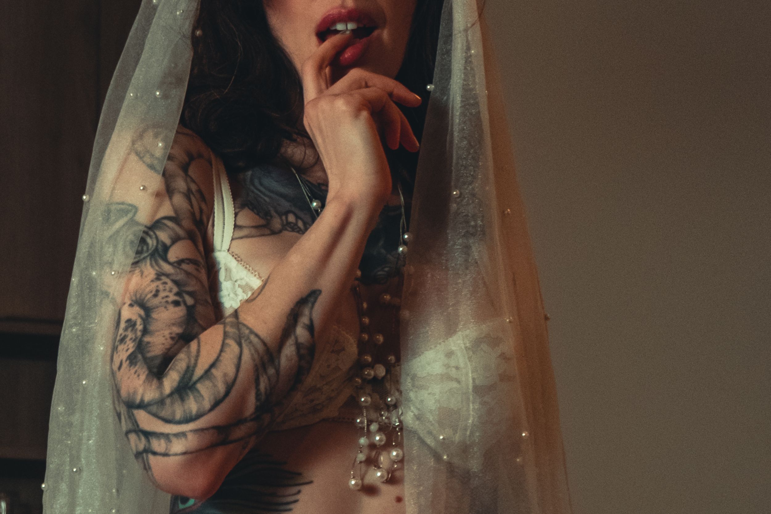 Delicate bridal veil with crystal beading frames a tattooed arm in moody lighting. bridal boudoir