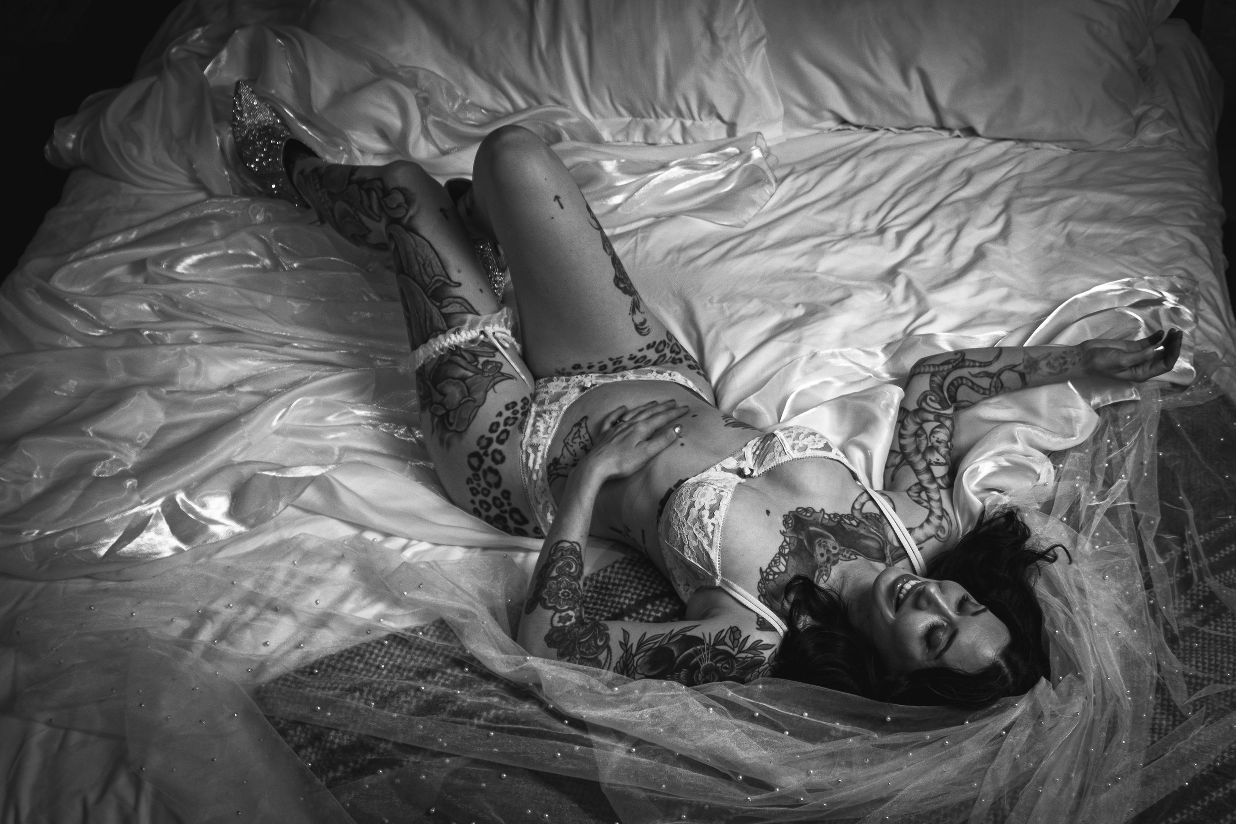 Dramatic black and white boudoir photograph with textured bedding and delicate lace details. bridal boudoir