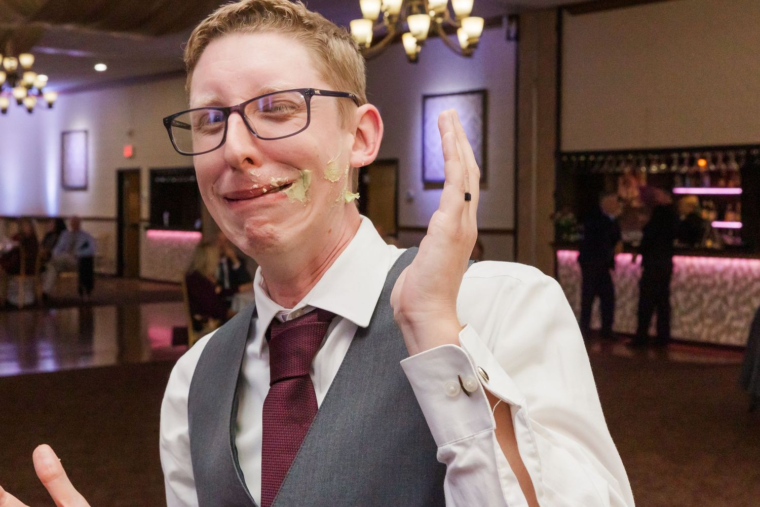 Wedding guest in formal attire smiling and gesturing at a reception venue.