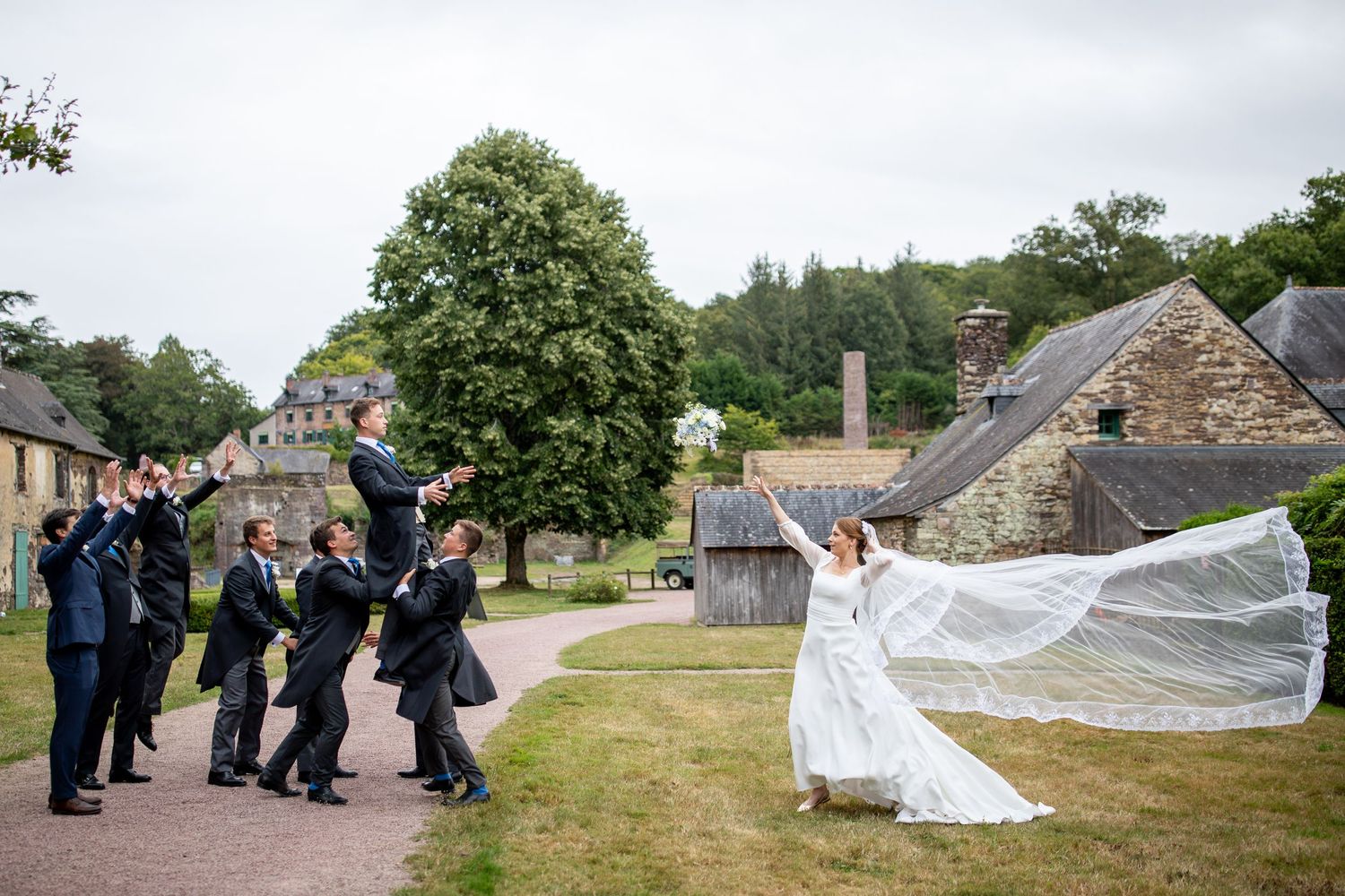 photographie de mariage femme lançant son bouquet avec son voile dans le vent couple heureux