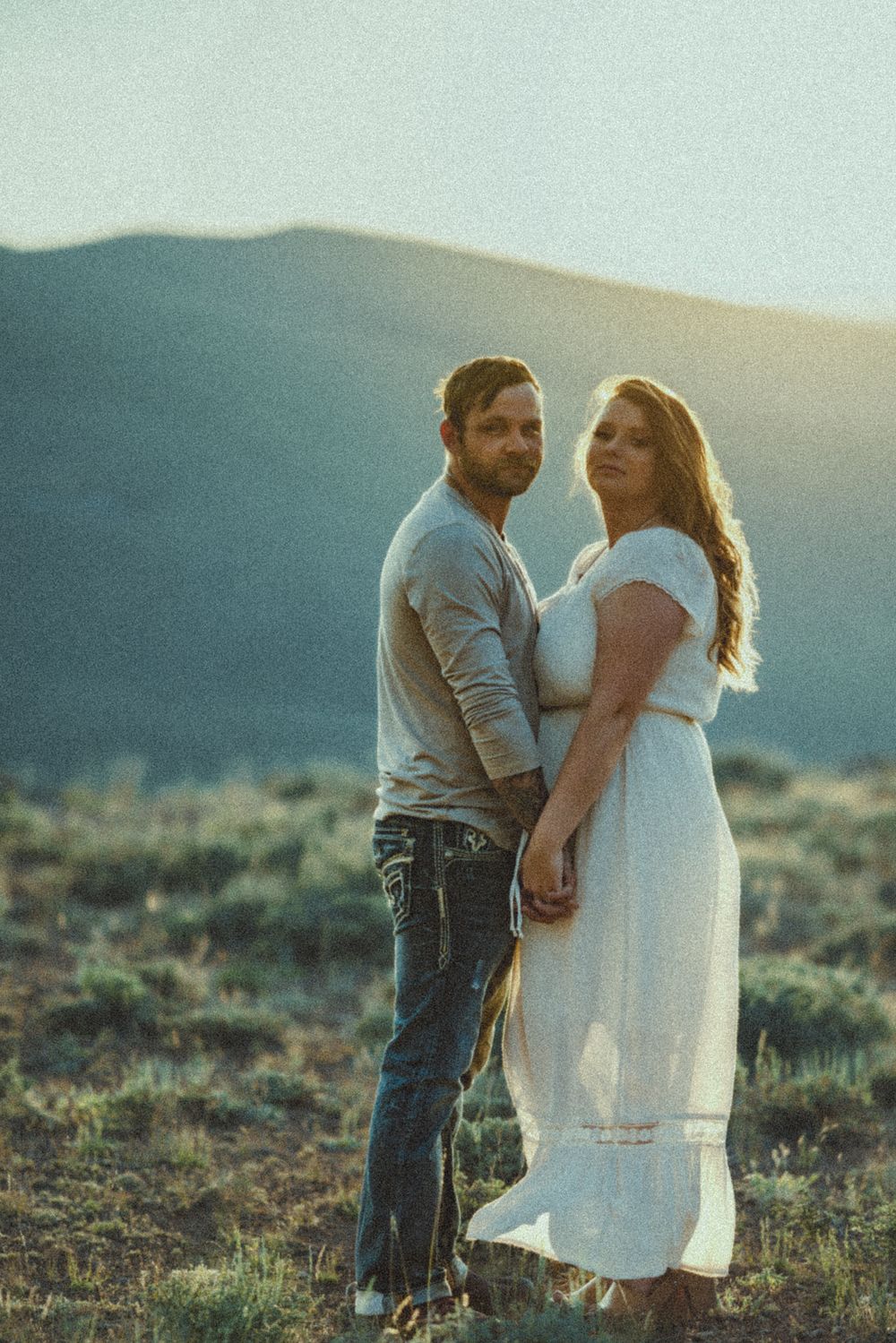 Two people in love embrace on a desert hillside during sunset.