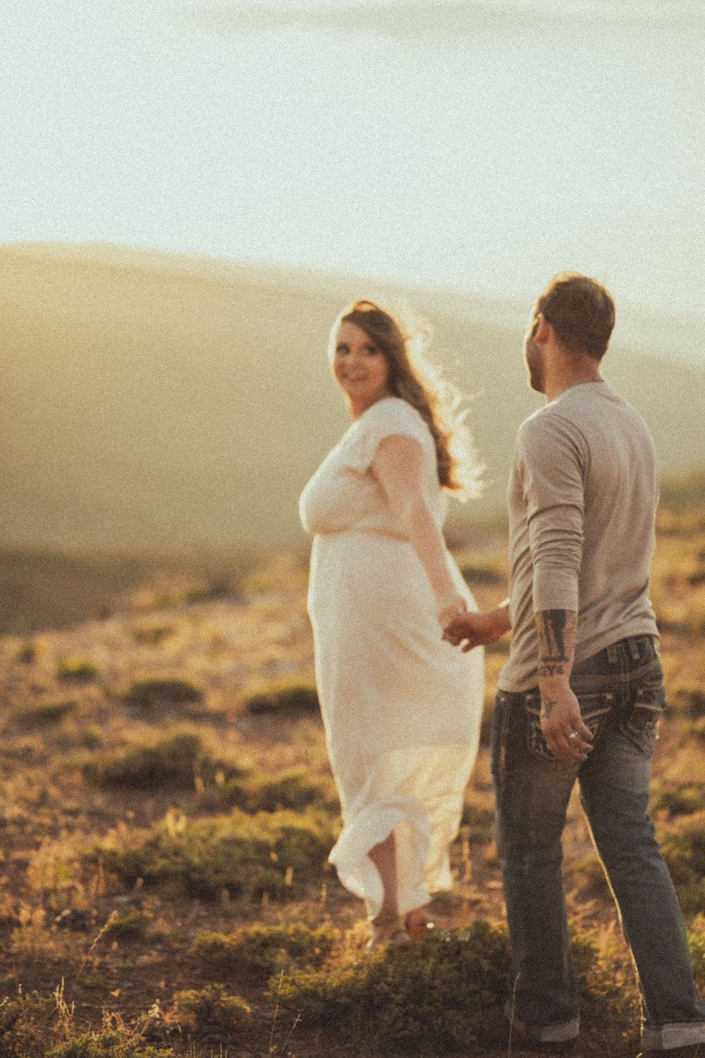 A romantic couple walks together in golden sunlight on a desert hillside.