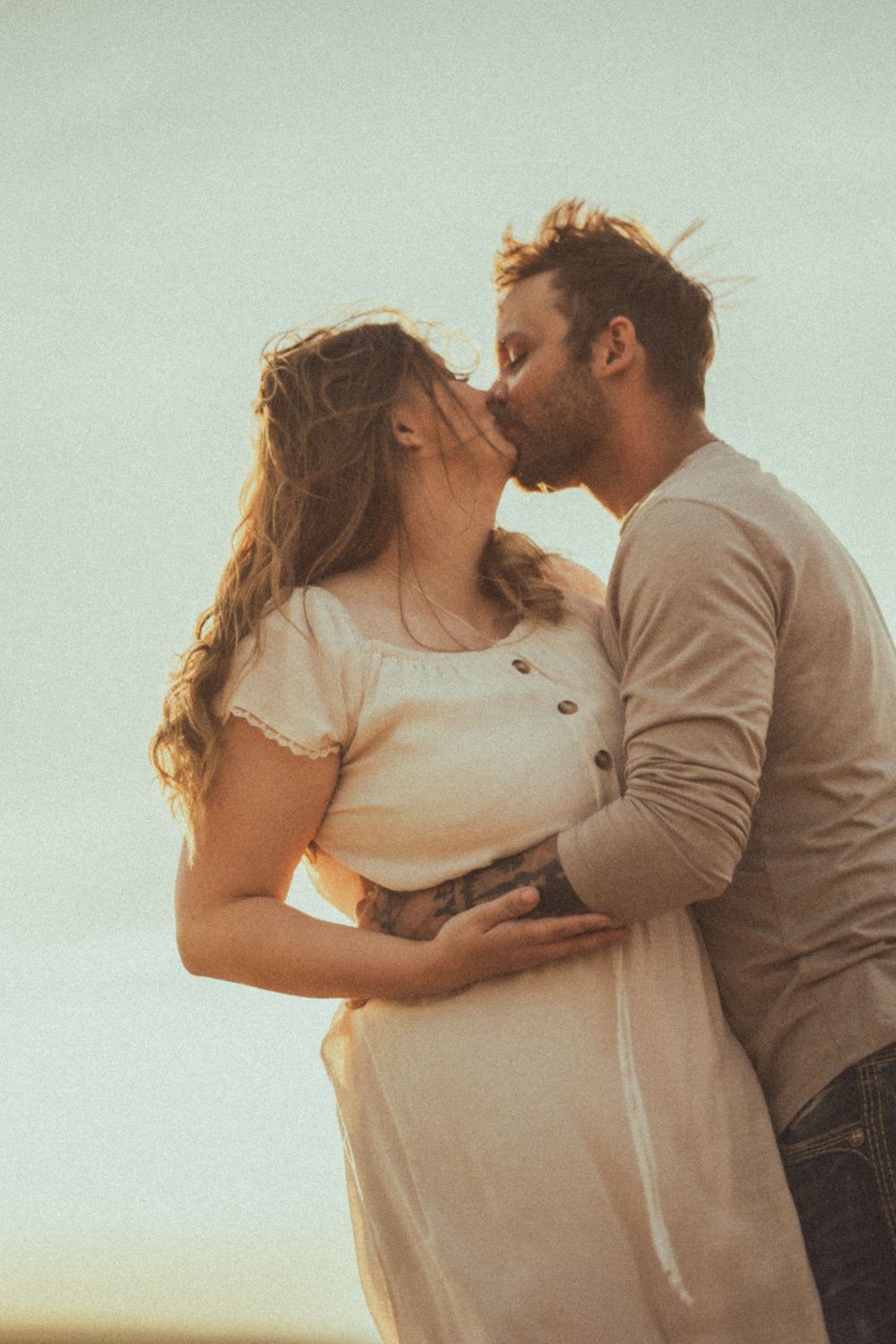 Romantic couple sharing a tender kiss at sunset in soft lighting against a dreamy background.