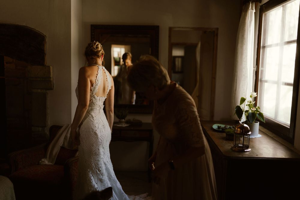 Elegant lace wedding dress being adjusted in a sunlit room.