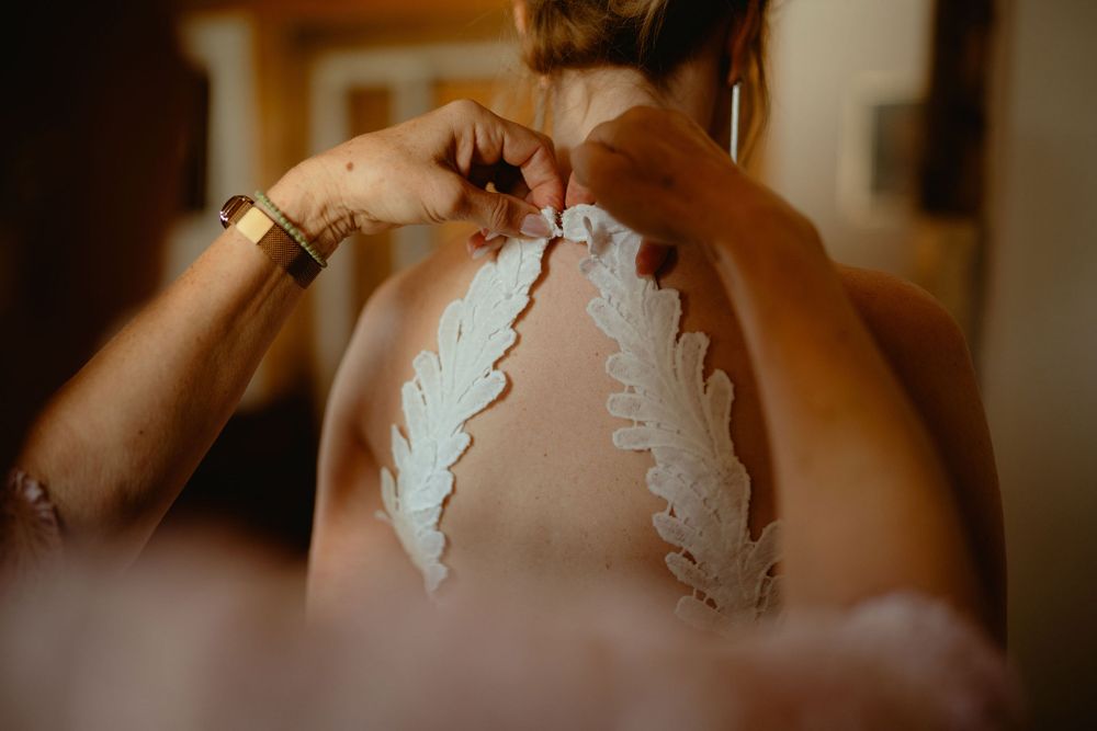 Close-up of hands fastening the back of a detailed lace wedding gown.