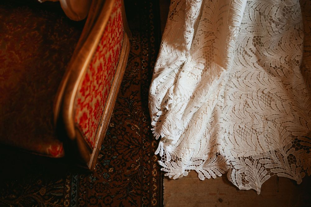 Detail shot of lace wedding dress hem next to red velvet furniture.