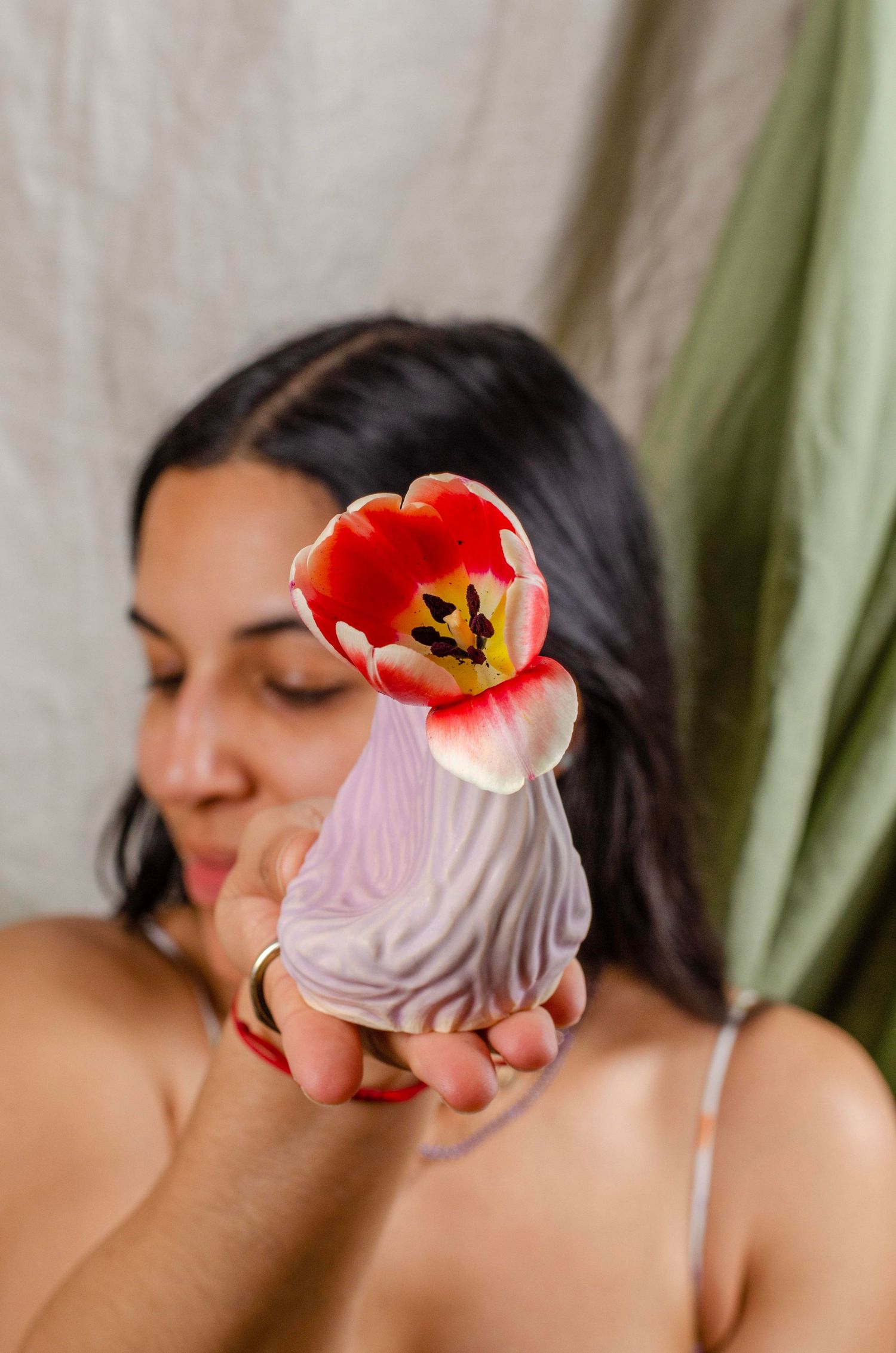 A red tulip flower rests against a handheld decorative ceramic vase with purple swirls.