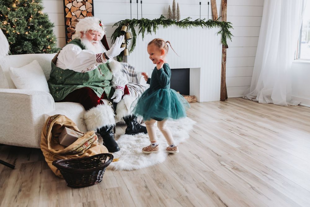 Children play and crawl on a light wooden floor in a bright white room decorated with holiday greenery.
