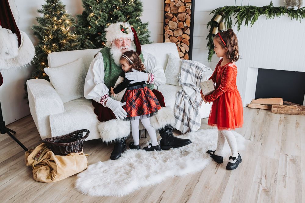Children in holiday outfits sit on the floor opening Christmas presents near a decorated tree and stockings.
