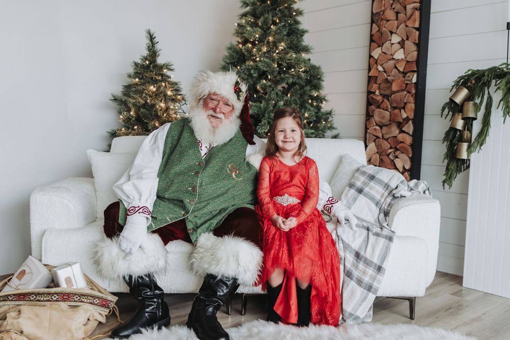 A festive Christmas photo session featuring a decorated evergreen tree and white chairs in a bright studio setting.