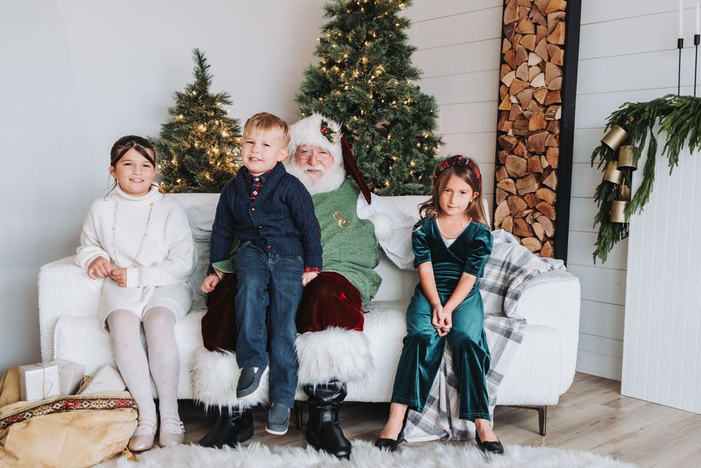 Family members sit together on white chairs in front of a decorated Christmas tree and rustic wood wall.