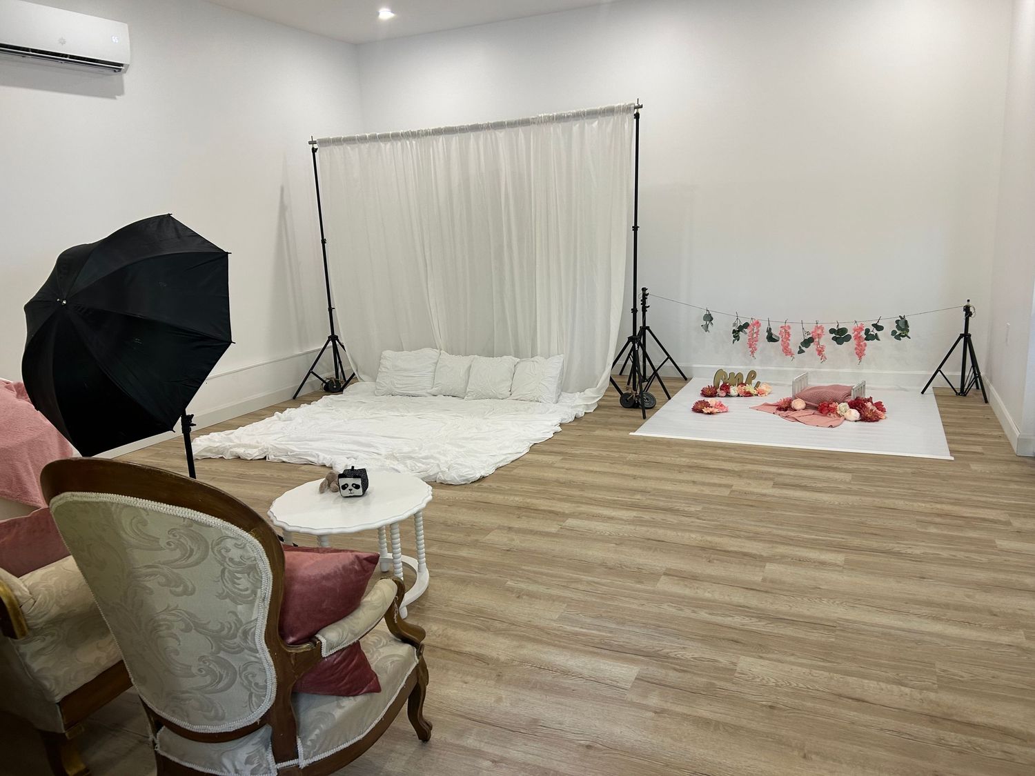 Professional photo studio setup with white backdrop, lighting equipment, and vintage chair on wooden flooring.