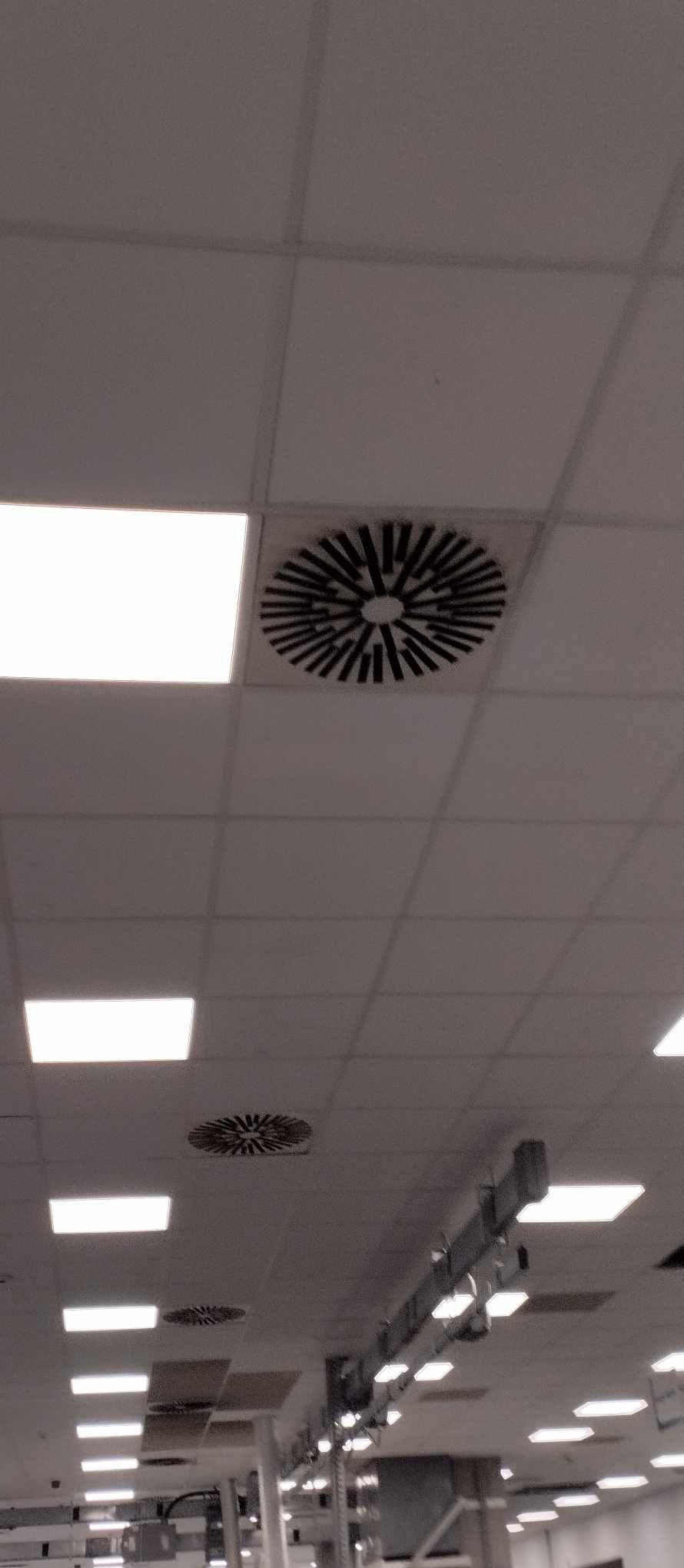 Commercial ceiling with fluorescent lights and circular air vents in a grid pattern.