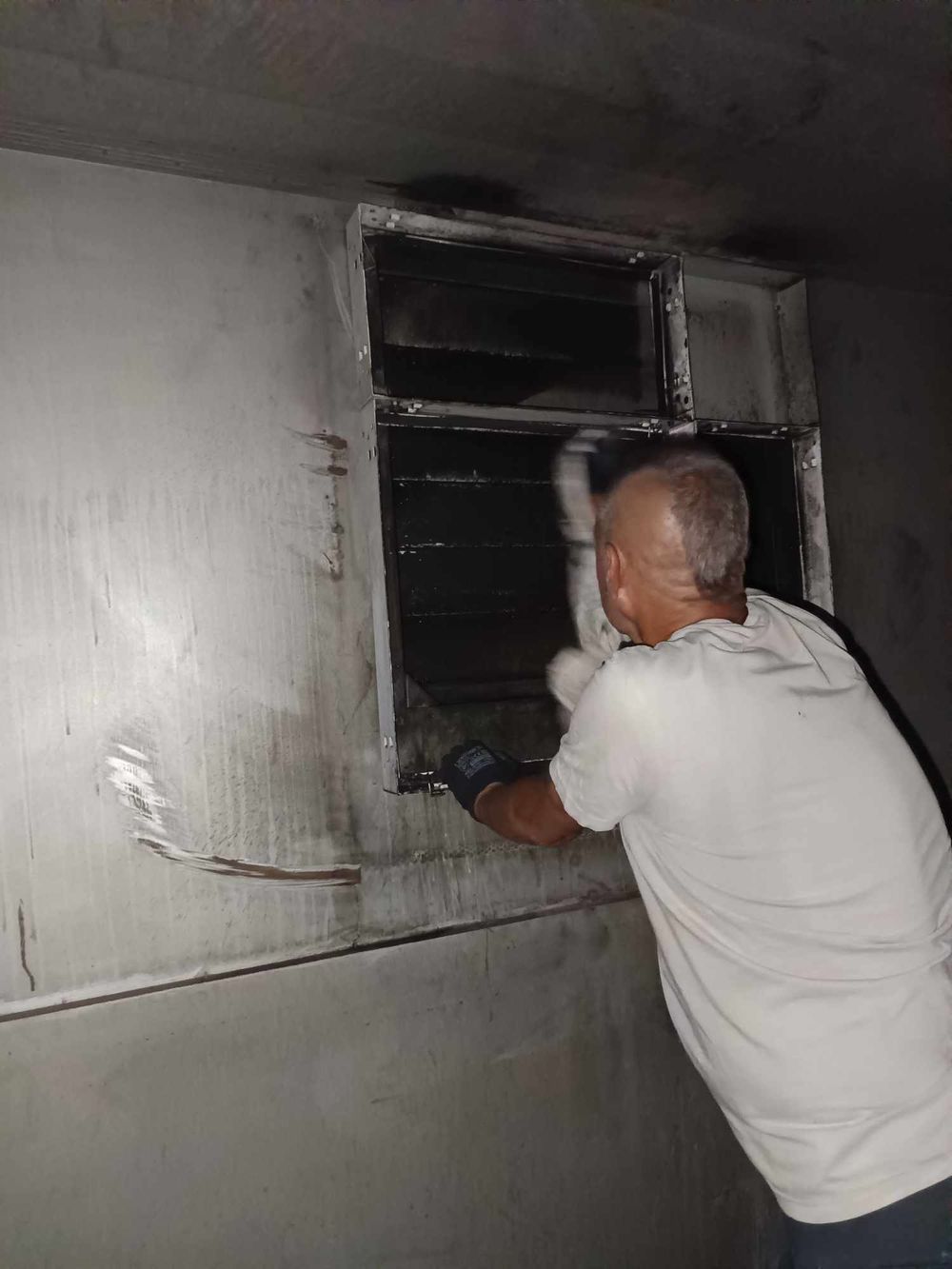 Maintenance worker inspecting a dark ventilation duct or crawl space with a flashlight.