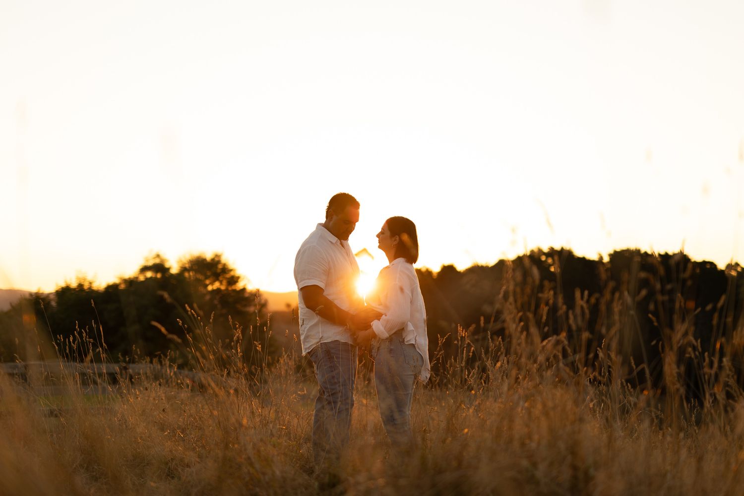 Silhouetted couple embraces in golden sunlit field during sunset creating romantic atmosphere.