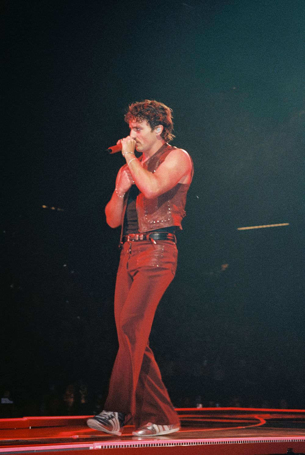 A performer in a red jumpsuit energetically dances and moves across a stage during a dynamic concert performance.