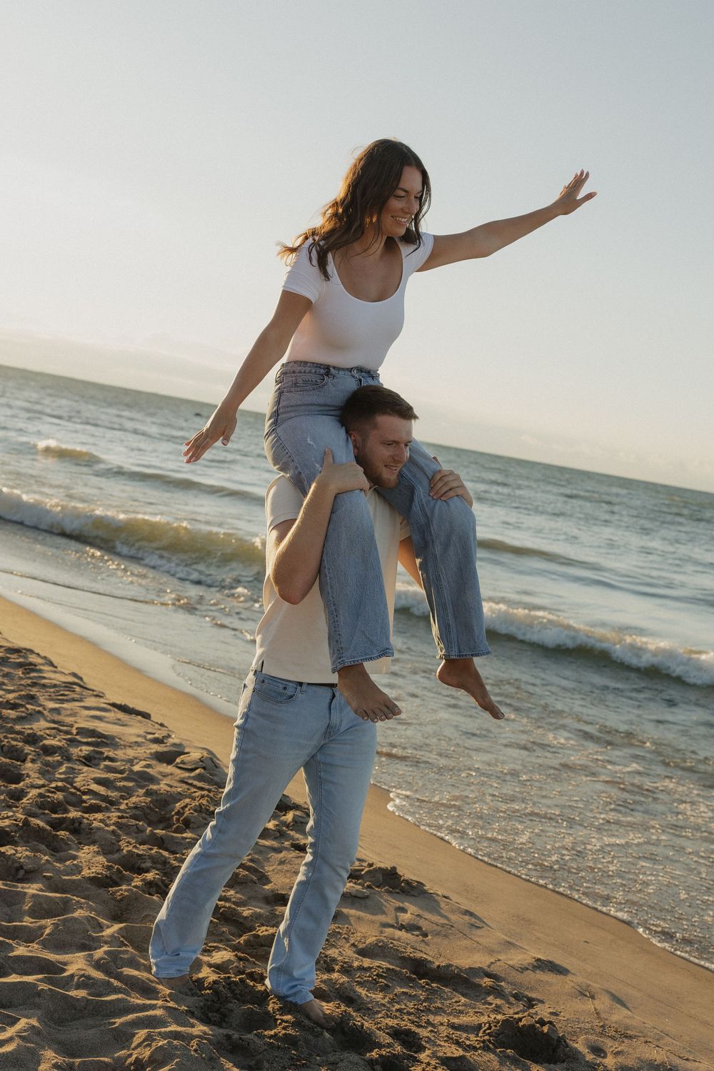 Playful couple enjoying a romantic moment on a sandy beach at sunset with ocean waves in the background.