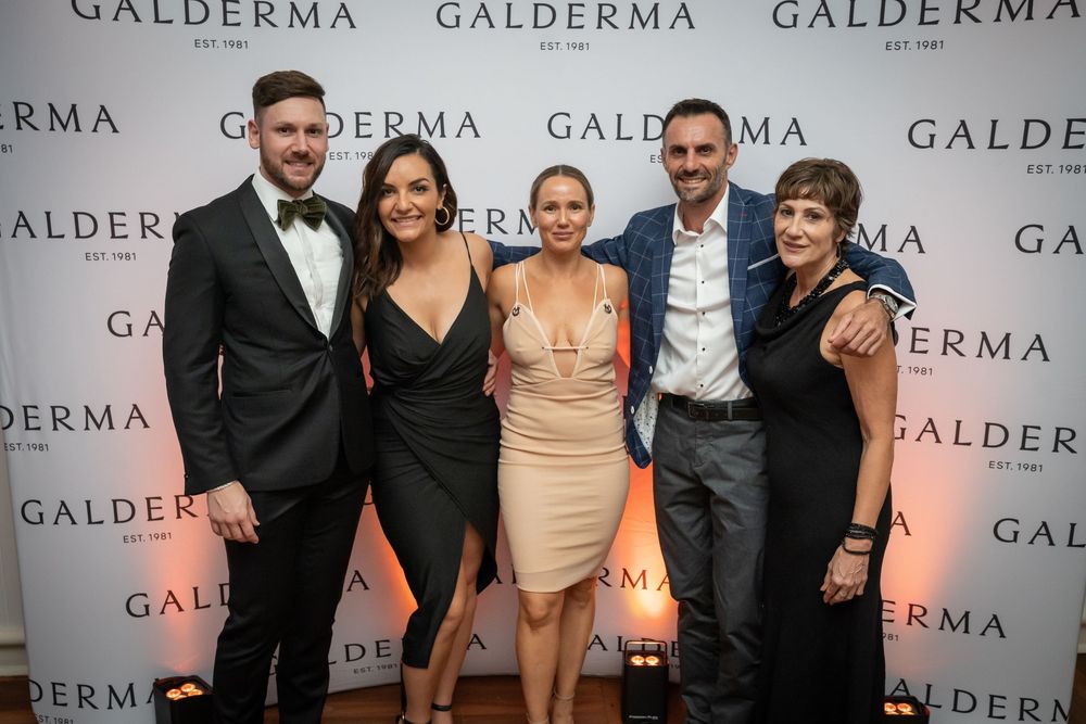 A group of people pose together at a Galderma branded event with repeating logo wall backdrop.